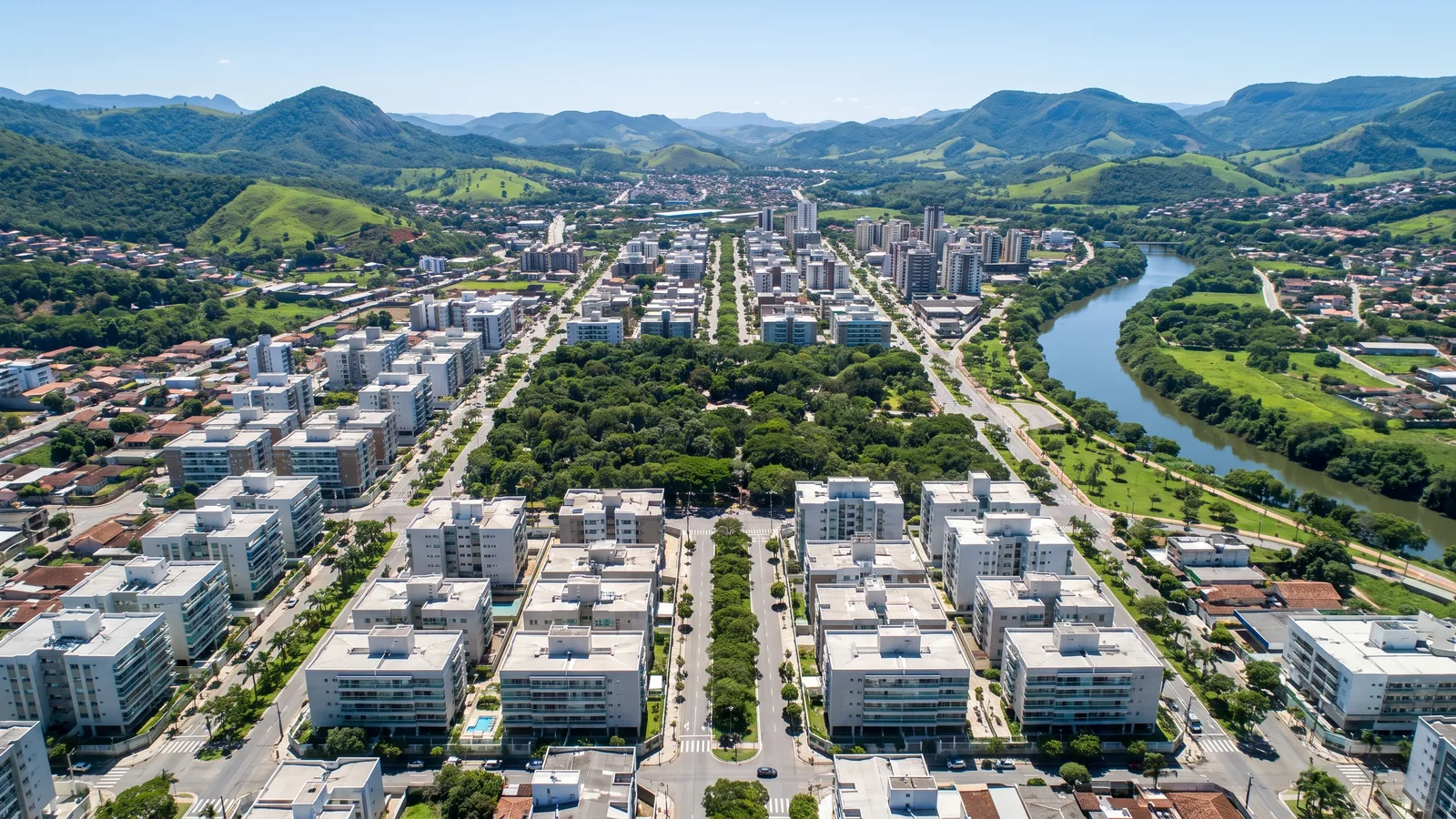 Vista aérea diurna de cidade planejada num vale entre montanhas, com avenidas largas arborizadas, prédios modernos, parque e rio